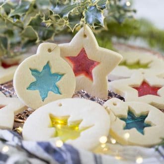 Stained glass cookies hanging from holly branches.