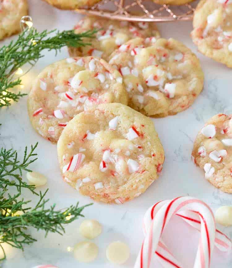 A group of white chocolate peppermint cookies next to candy canes and evergreen clippings.