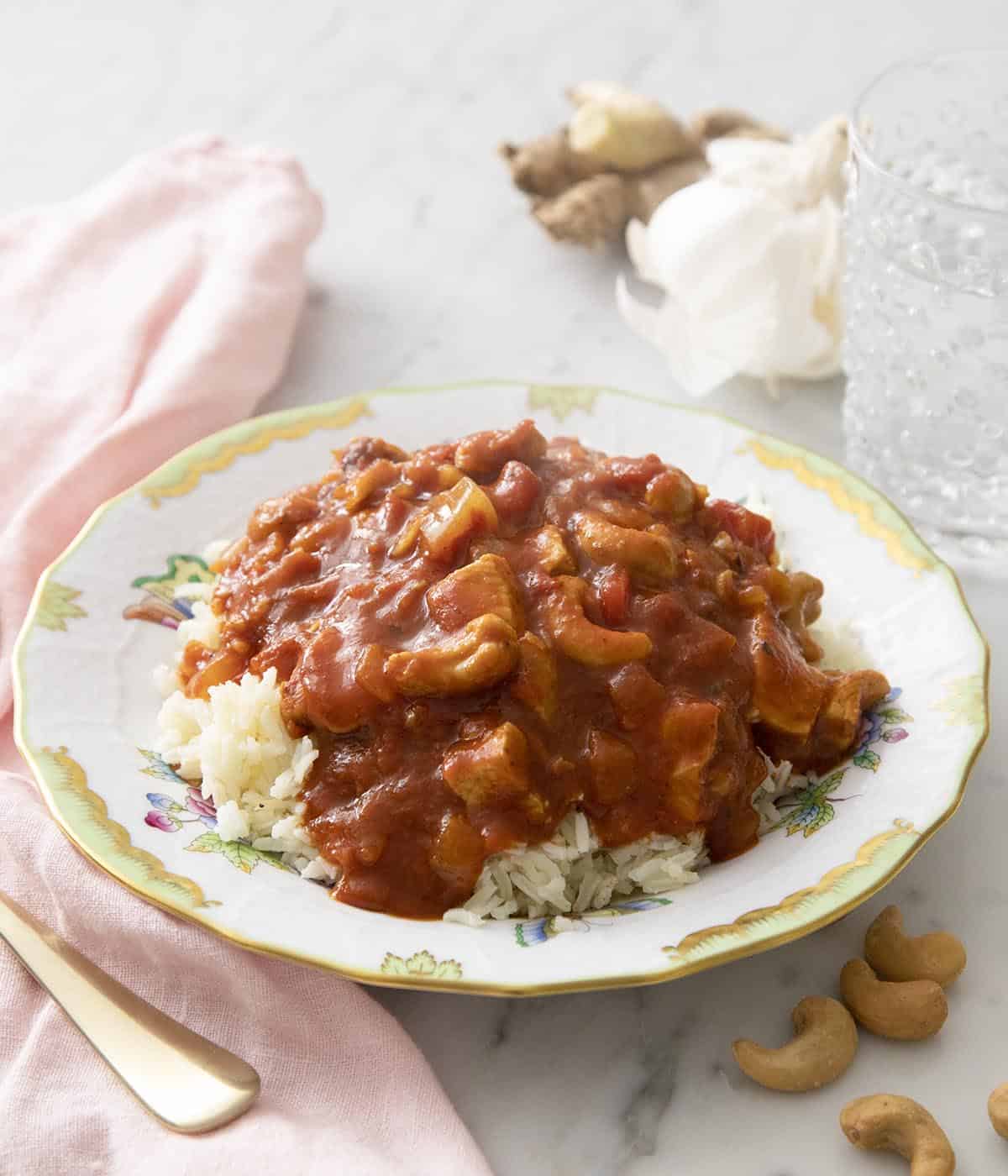 A plate of butter chicken next to a glass of water.