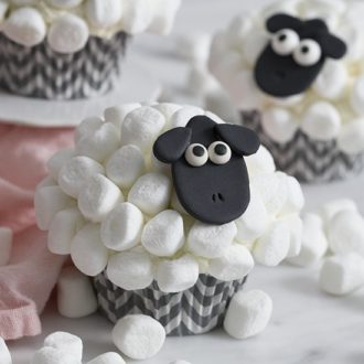A closeup photo of a sheep cupcake with a black fondant face and mini marshmallow wool.