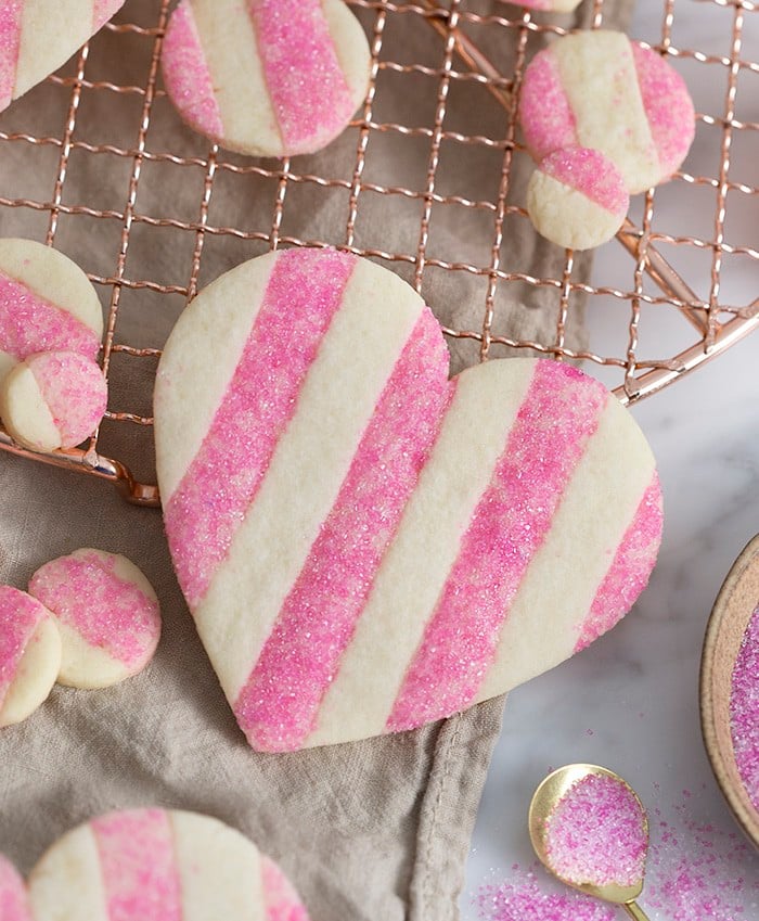 A photo of a pink and white striped Valentine's Day Heart Cookie with sparkling pink sanding sugar on the pink stripes 