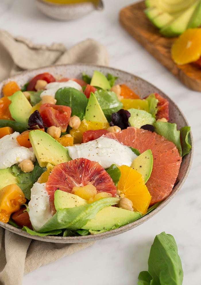 A photo of an avocado salad with various citrus premiums and burrata in a white bowl