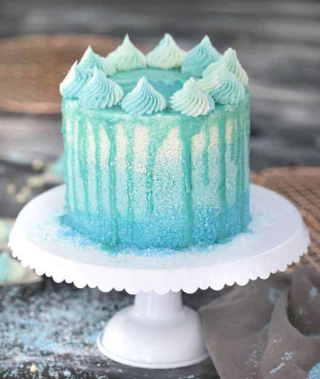 A winter wonderland cake covered in blue sparkles with a blue drip.