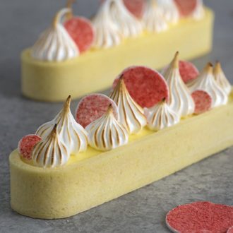A close up image of a lemon curd tart with pink circles on top and toasted meringue dollops.