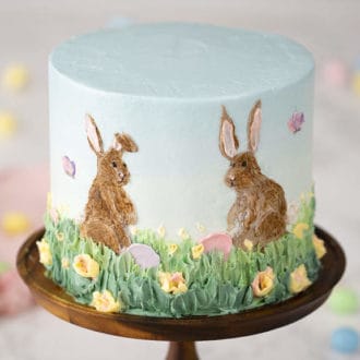 An easter bunny cake on a cake stand featuring hand painted bunnies