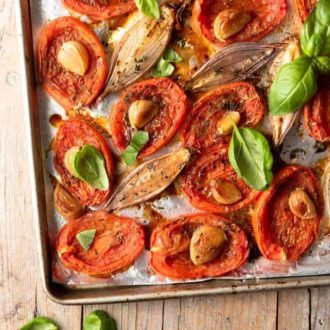 Close up shot of a baking sheet with oven roasted tomatoes and shallots on it.