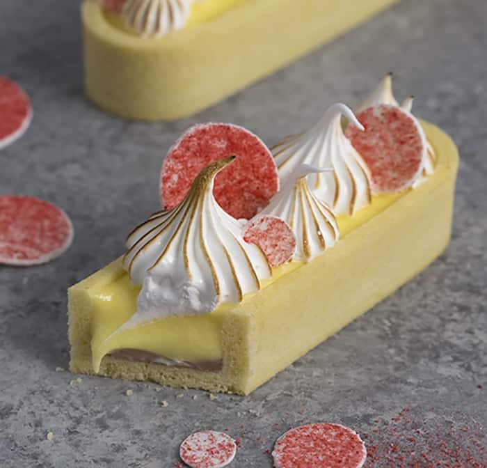 A close up image of a lemon curd tart with pink circles on top and toasted meringue dollops.