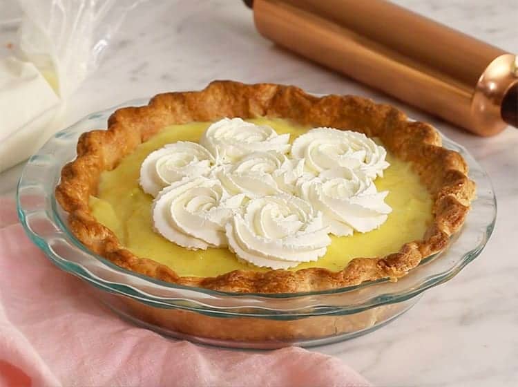 A cream pie topped with rosettes of whipped cream on a white marble table