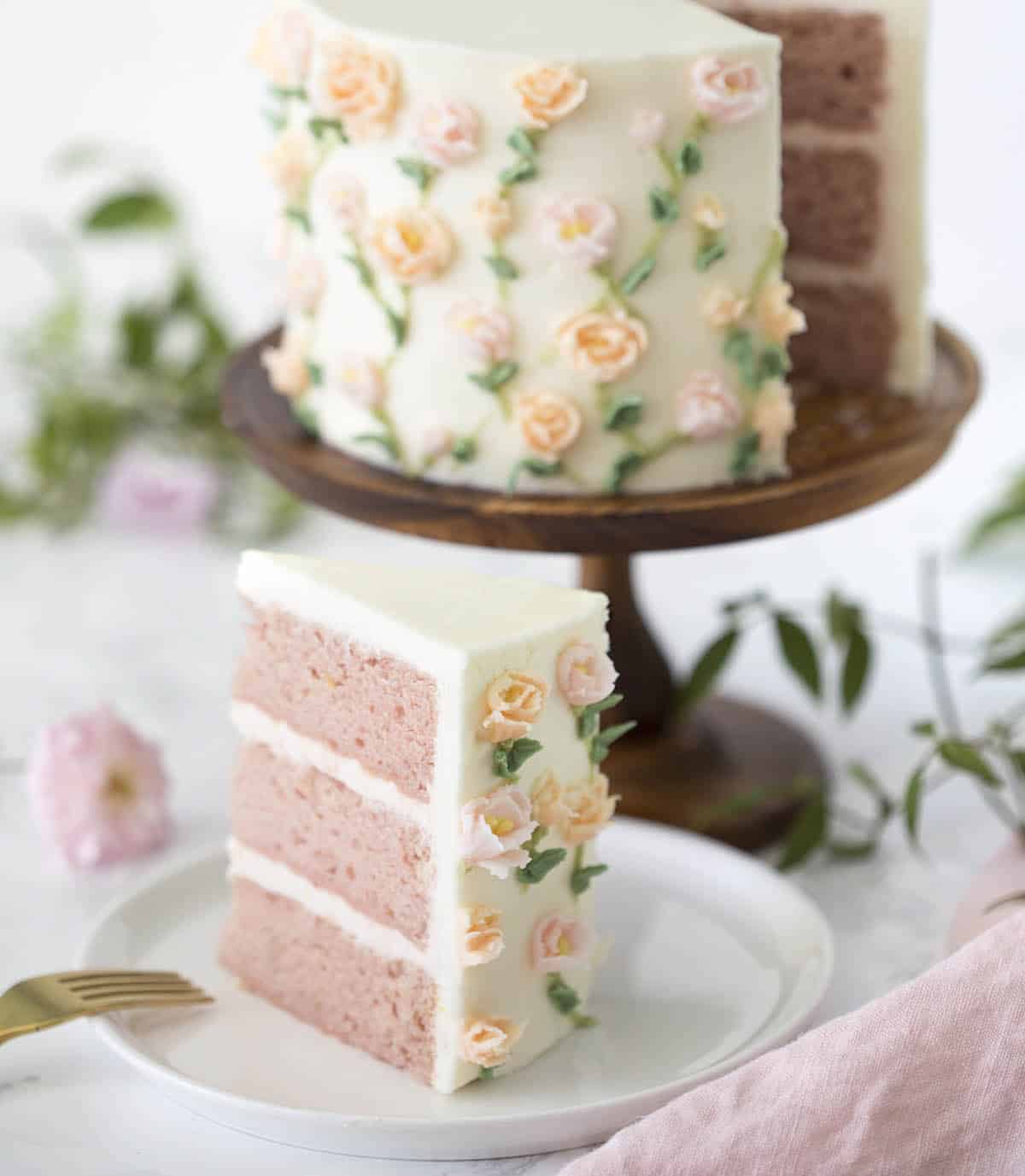 A pink cake with snall roses painted on using buttercream frosting.