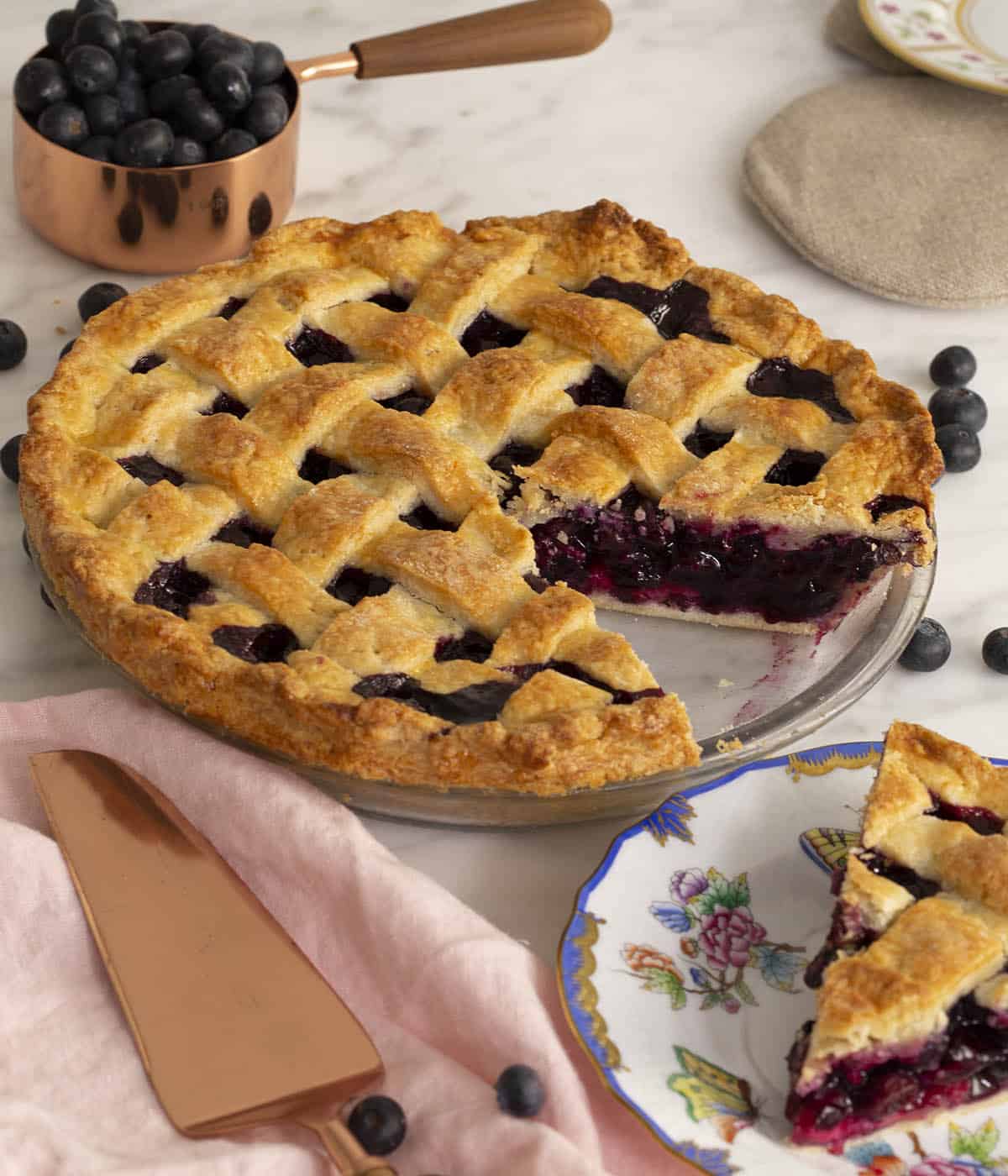 Blueberry pie in a glass baking dish with a slice cut out and plated on the side.