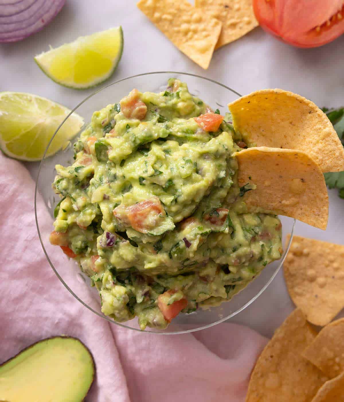 An overhead shot a bowl of guacamole with limes and tortilla chips at the side.