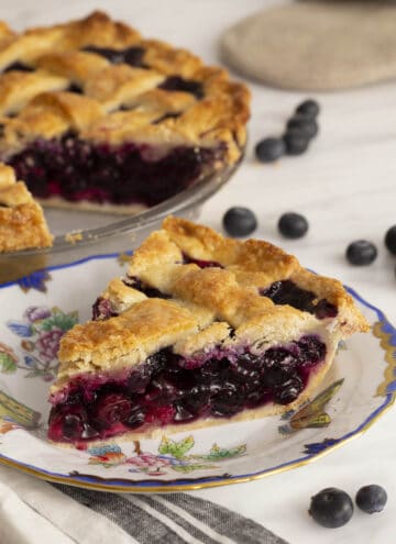 A lattice-topped blueberry pie with a piece cut out in the foreground.