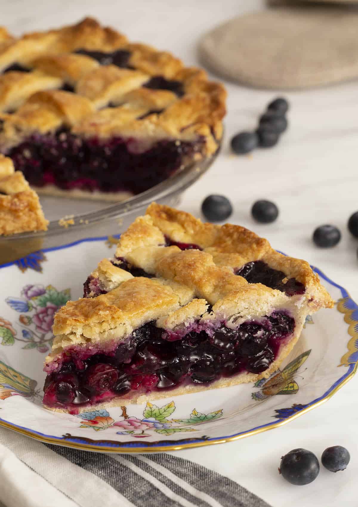 A lattice-topped blueberry pie with a piece cut out in the foreground.