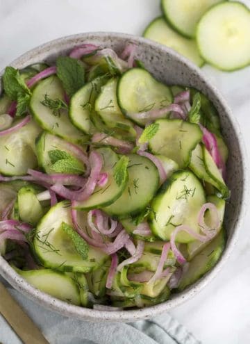 A bowl of cucumber salad with fresh dill and red onion slices.