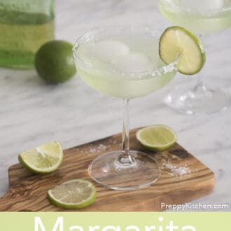 Pinterest graphic of a margarita cocktail in a stemmed glass. It sits on a wooden cutting board with lime slices scattered around.