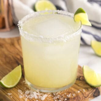 A margarita on the rocks with salt in a tumbler. Lime wedges scattered around.