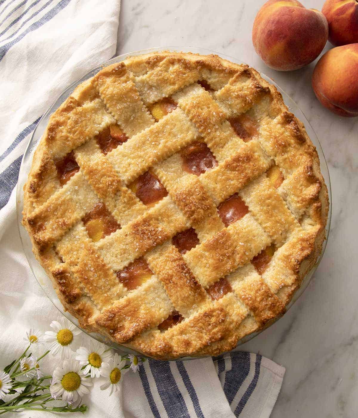An overhead view of a peach pie with a pastry lattice on a marble counter.