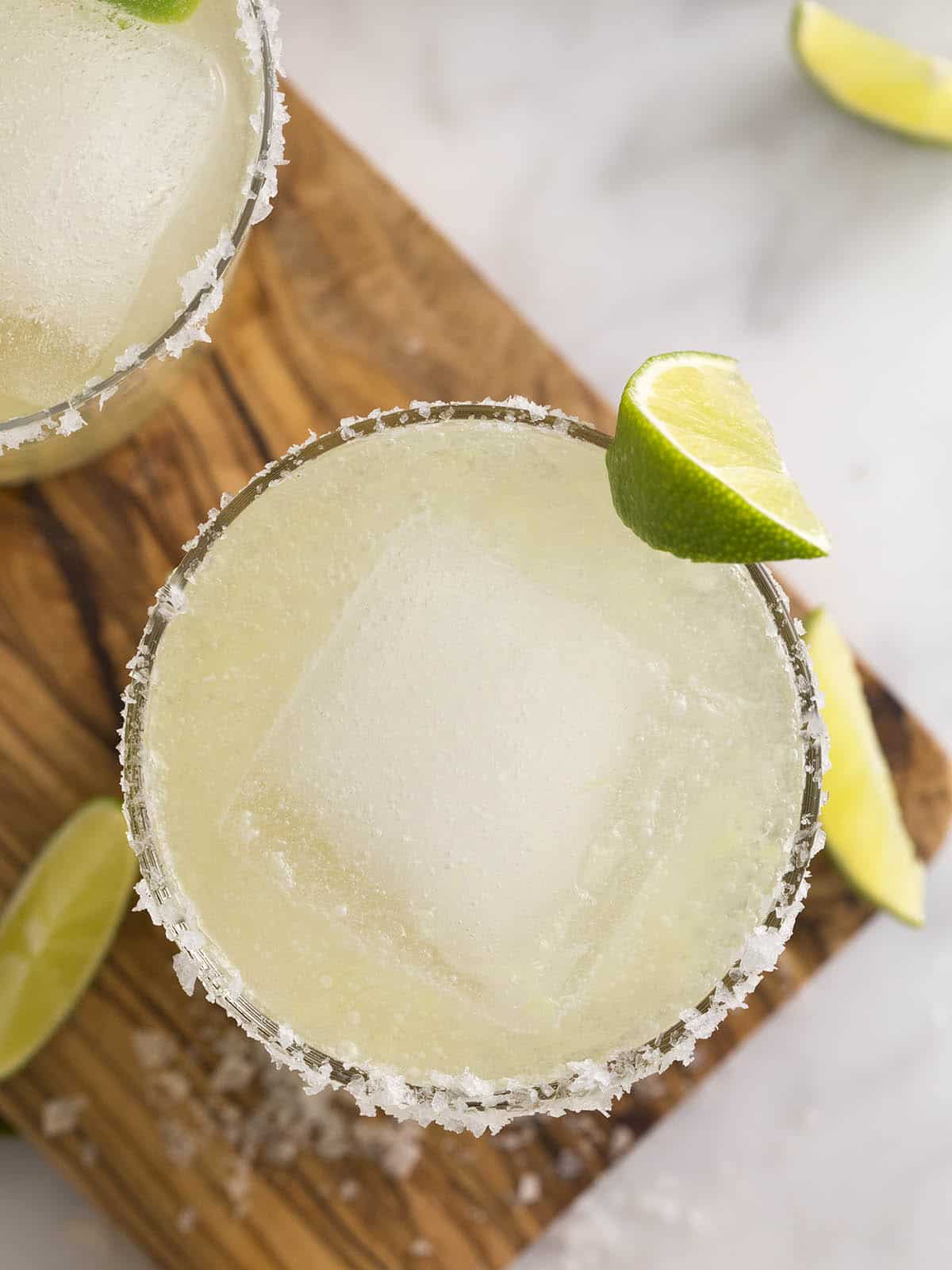Overhead view of a margarita on a wooden cutting board garnished with a lime wedge.