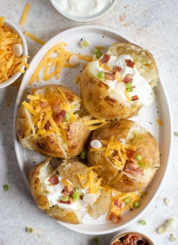 An overhead shot of instant pot baked potatoes on a serving plate with an assortment of toppings. More toppings in bowls off to the side.