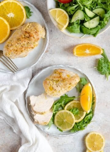 An overhead shot of Instant Pot chicken breasts on plates with greens and sliced oranges. A salad off on the side.
