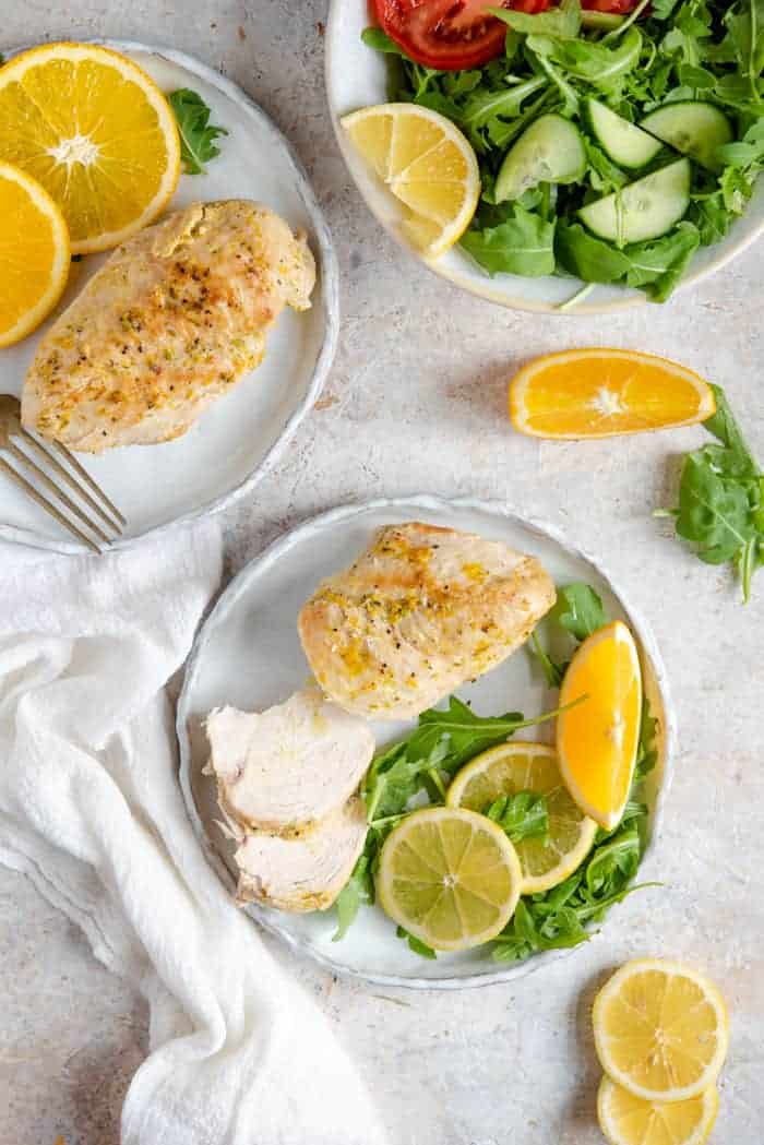 An overhead shot of Instant Pot chicken breasts on plates with greens and sliced oranges. A salad off on the side.