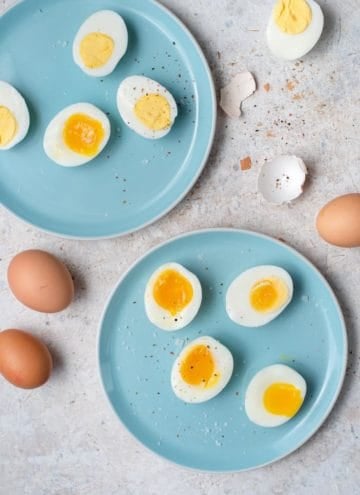 An overhead shot of hard boiled eggs and soft boiled eggs on two blue plates.