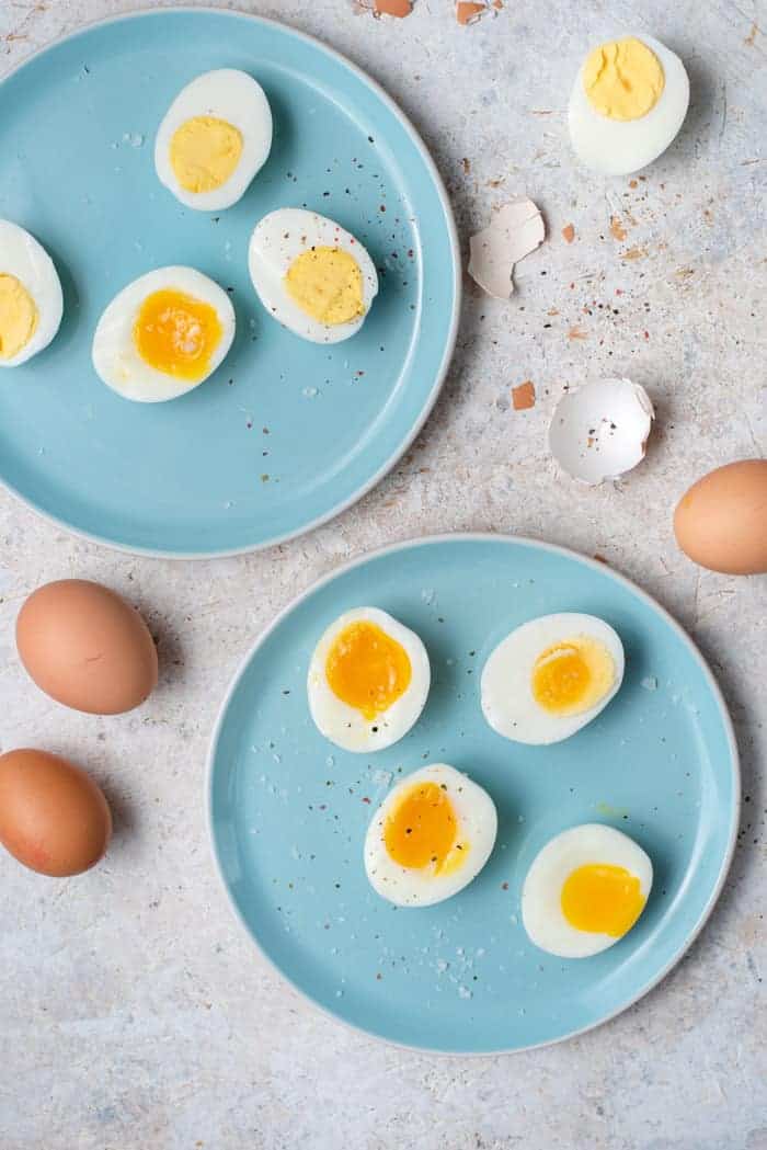 An overhead shot of hard boiled eggs and soft boiled eggs on two blue plates.
