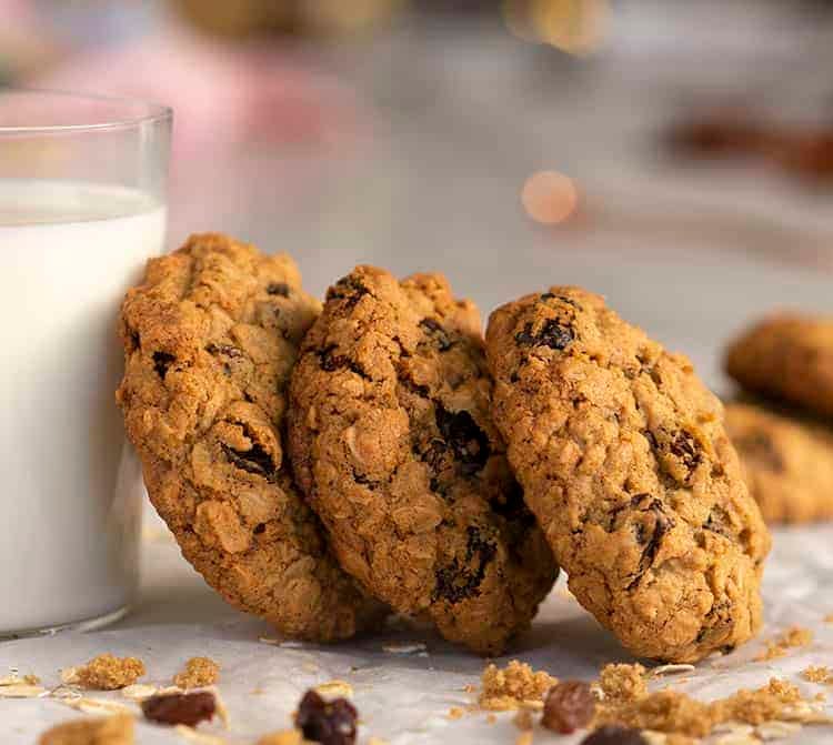 Oatmeal raisin cookies leaning a against a glass of milk.