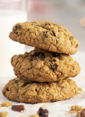 three oatmeal raisin cookies stacked next to a glass of milk