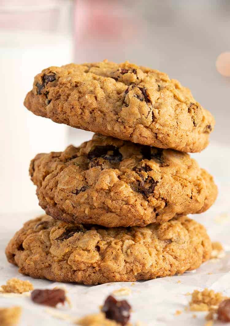 three oatmeal raisin cookies stacked next to a glass of milk