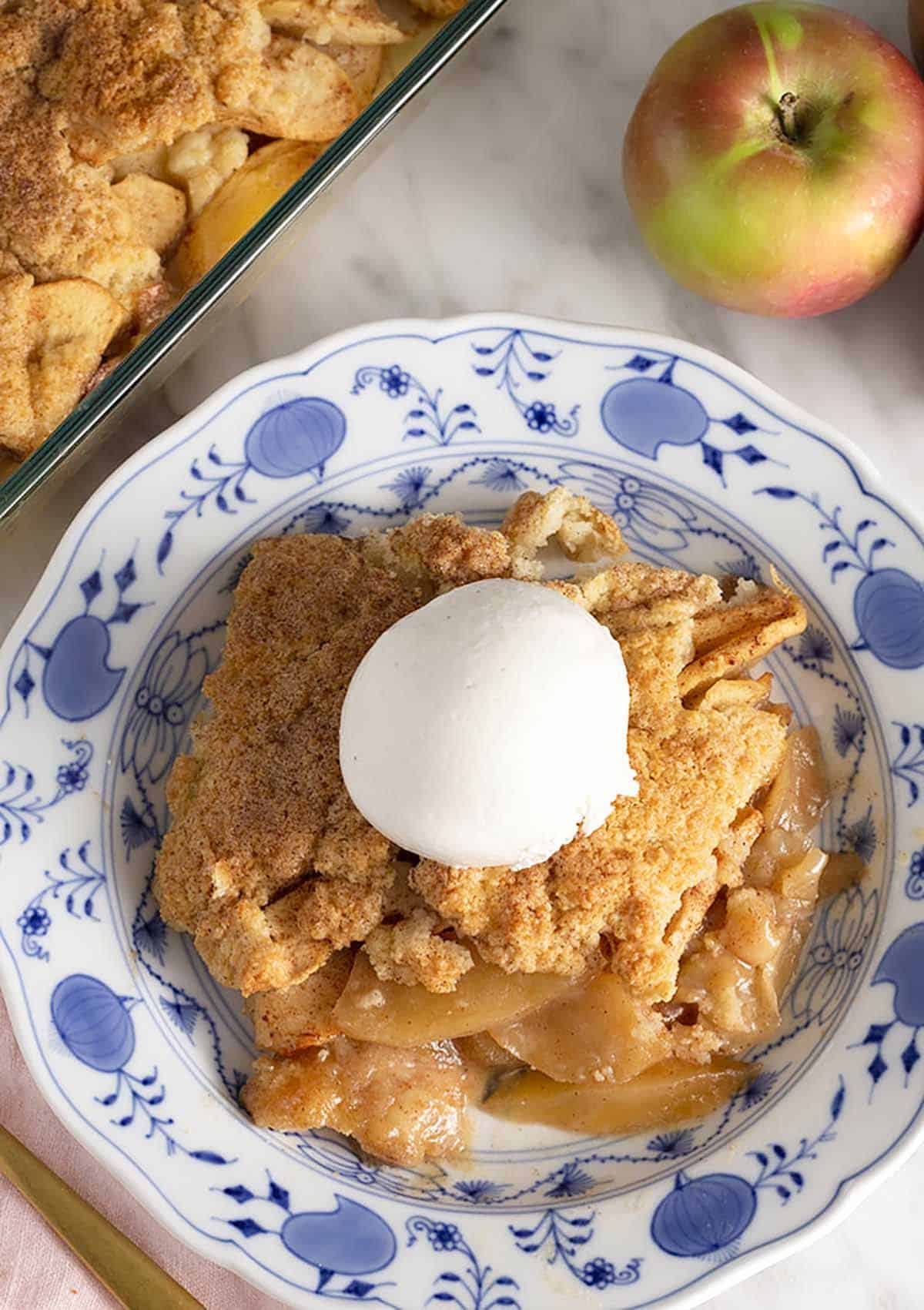 Overhead view of a plate with a serving of apple cobbler with a scoop of vanilla ice cream on top.