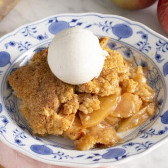 Apple cobbler on a plate with a scoop of vanilla ice cream.
