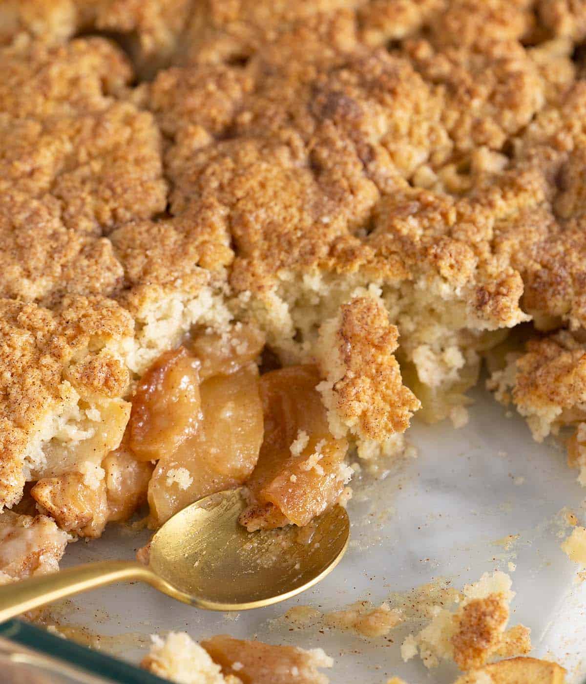 A glass dish of apple cobbler with a golden spoon.