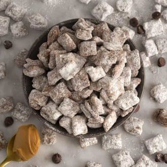 A bowl of puppy chow with chocolate chips scattered around on a marble table.