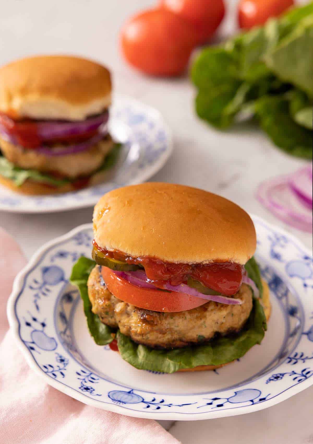 Turkey burgers on china plates with salad and tomatoes in the background