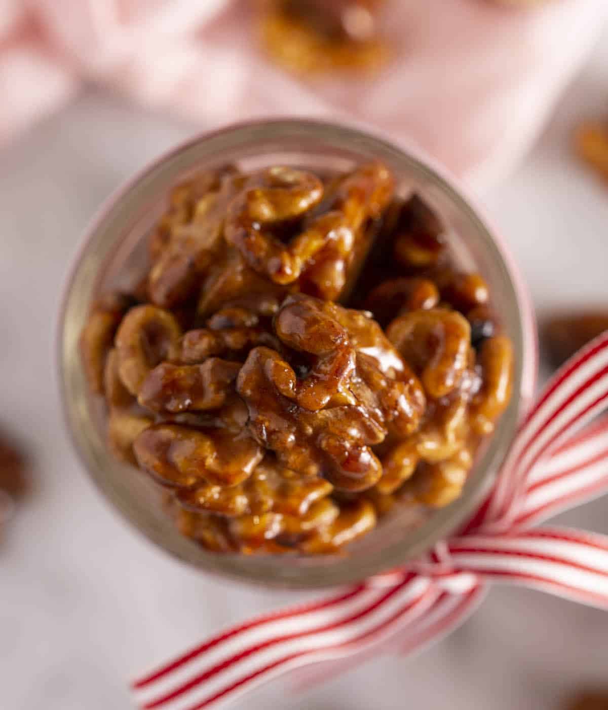 A top-down shot of candied walnuts in a glass jar with a bow tied around it.