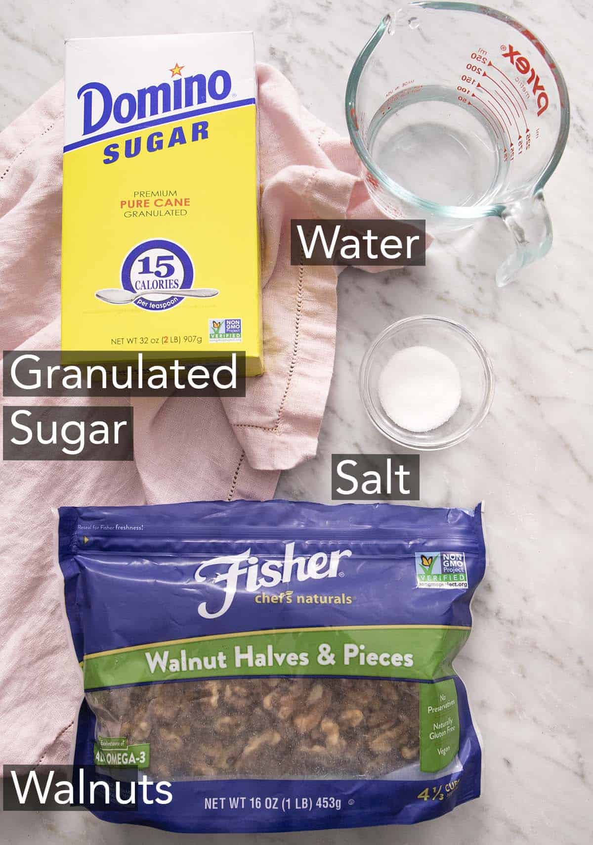 Ingredients to make candied walnuts with text labels on a marble counter.