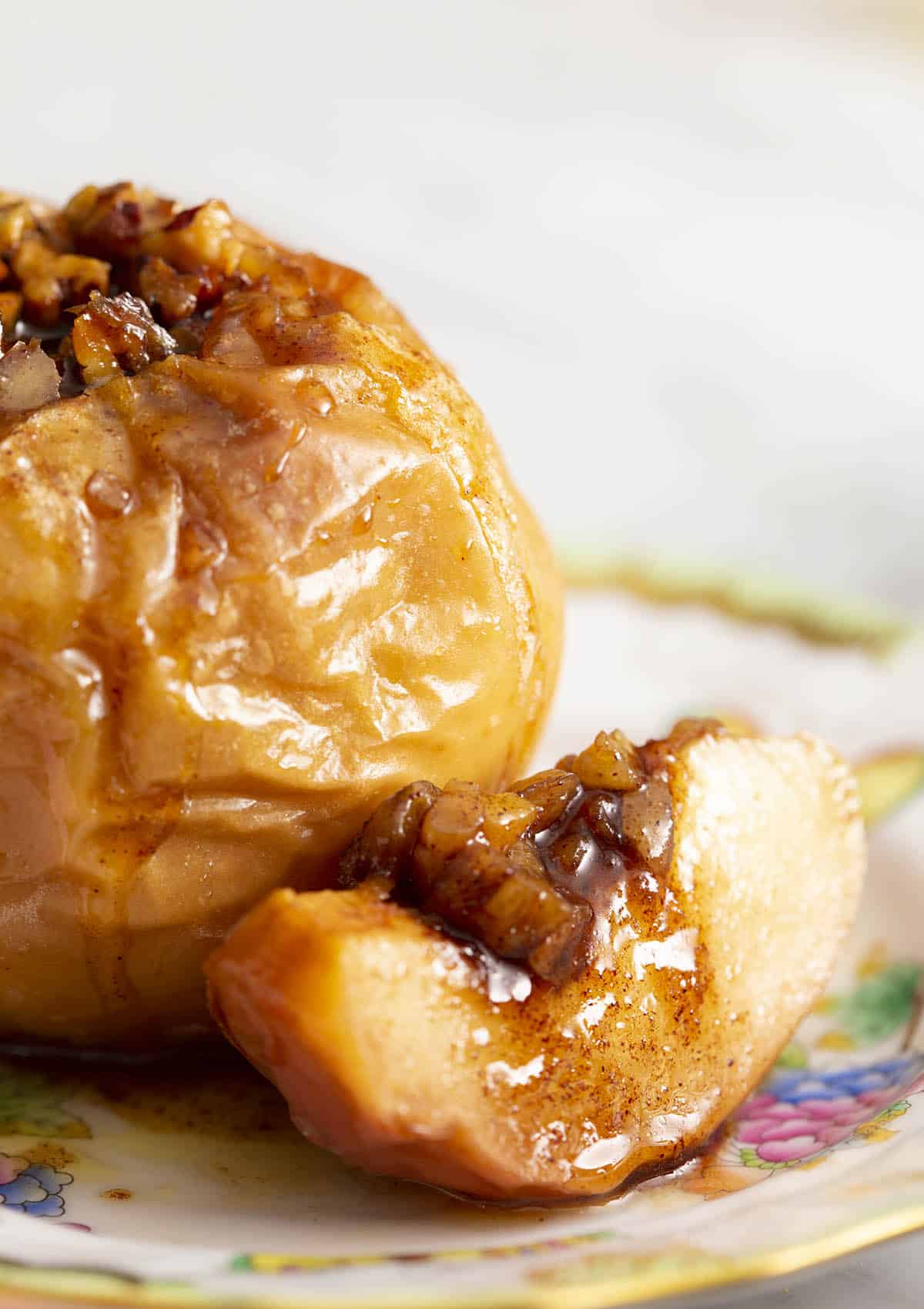A close up of a baked apple sitting on a plate with a slice beside it.