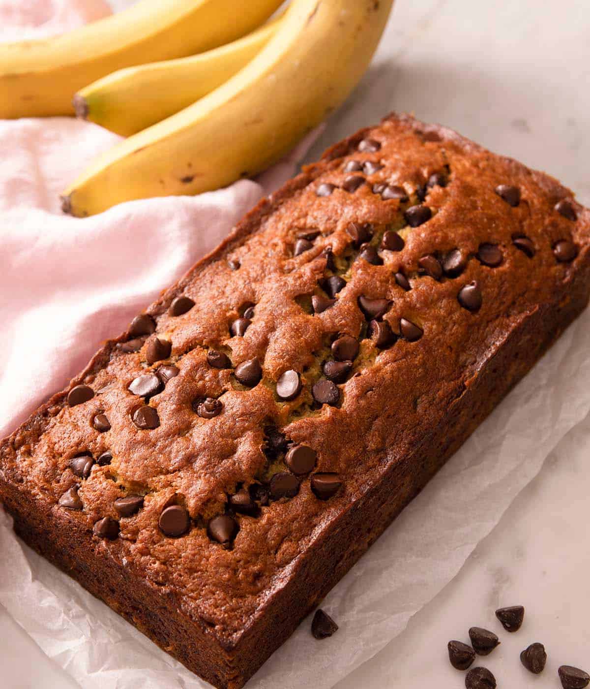 A loaf of chocolate chip banana bread on a work surface with chocolate chips scattered around.
