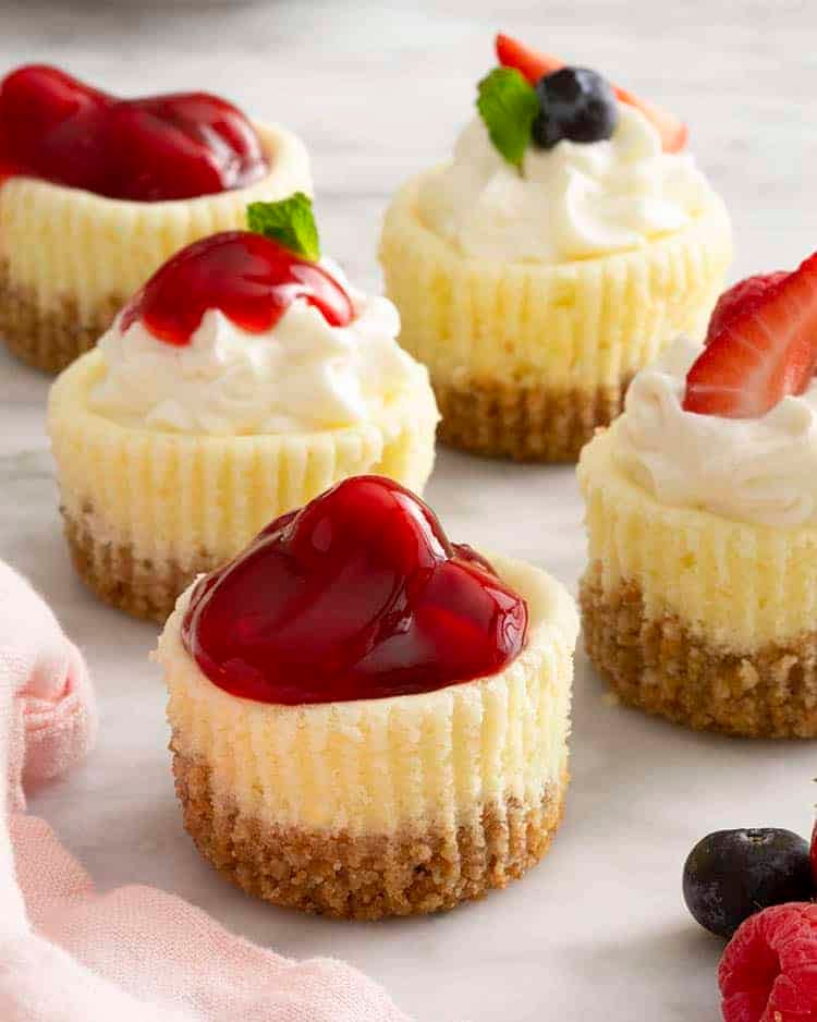 A group of mini cheesecakes on a marble surface. Each has different toppings.