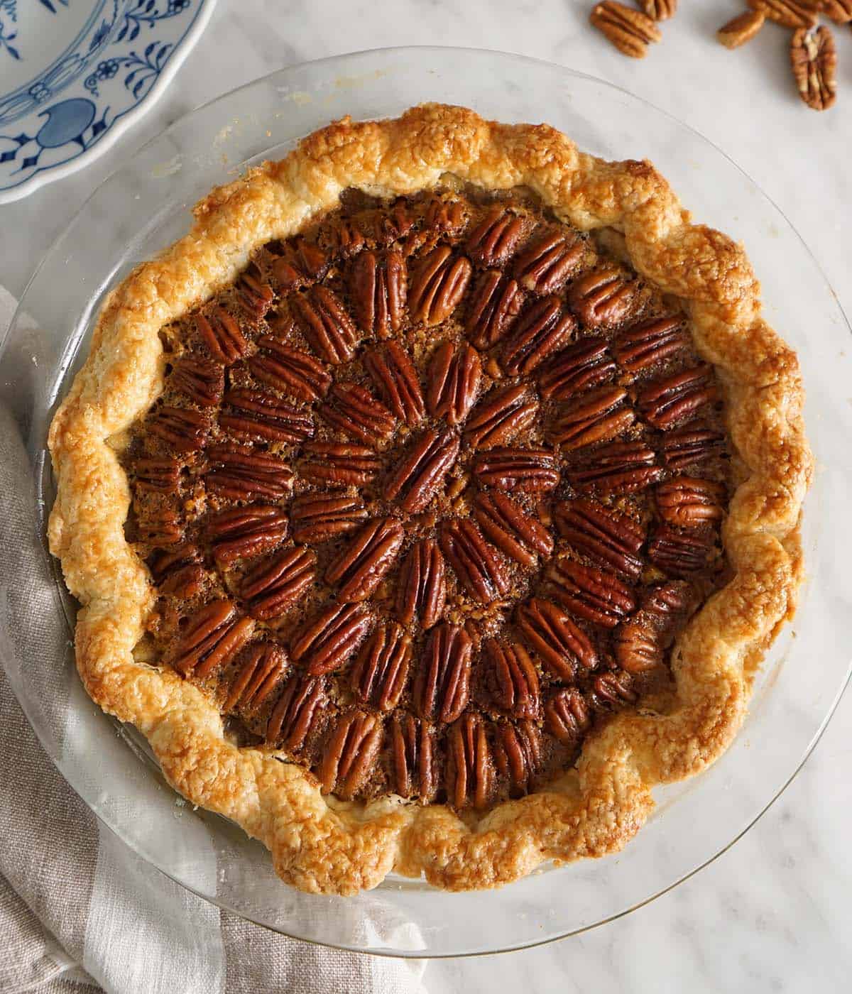 An overhead shot of a pecan pie on a white marble table.