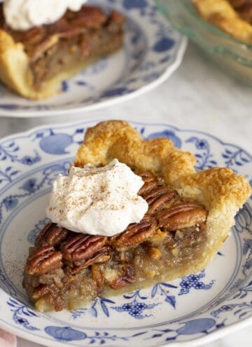 Two pieces of pecan pie on blue and white plates on a marble table.