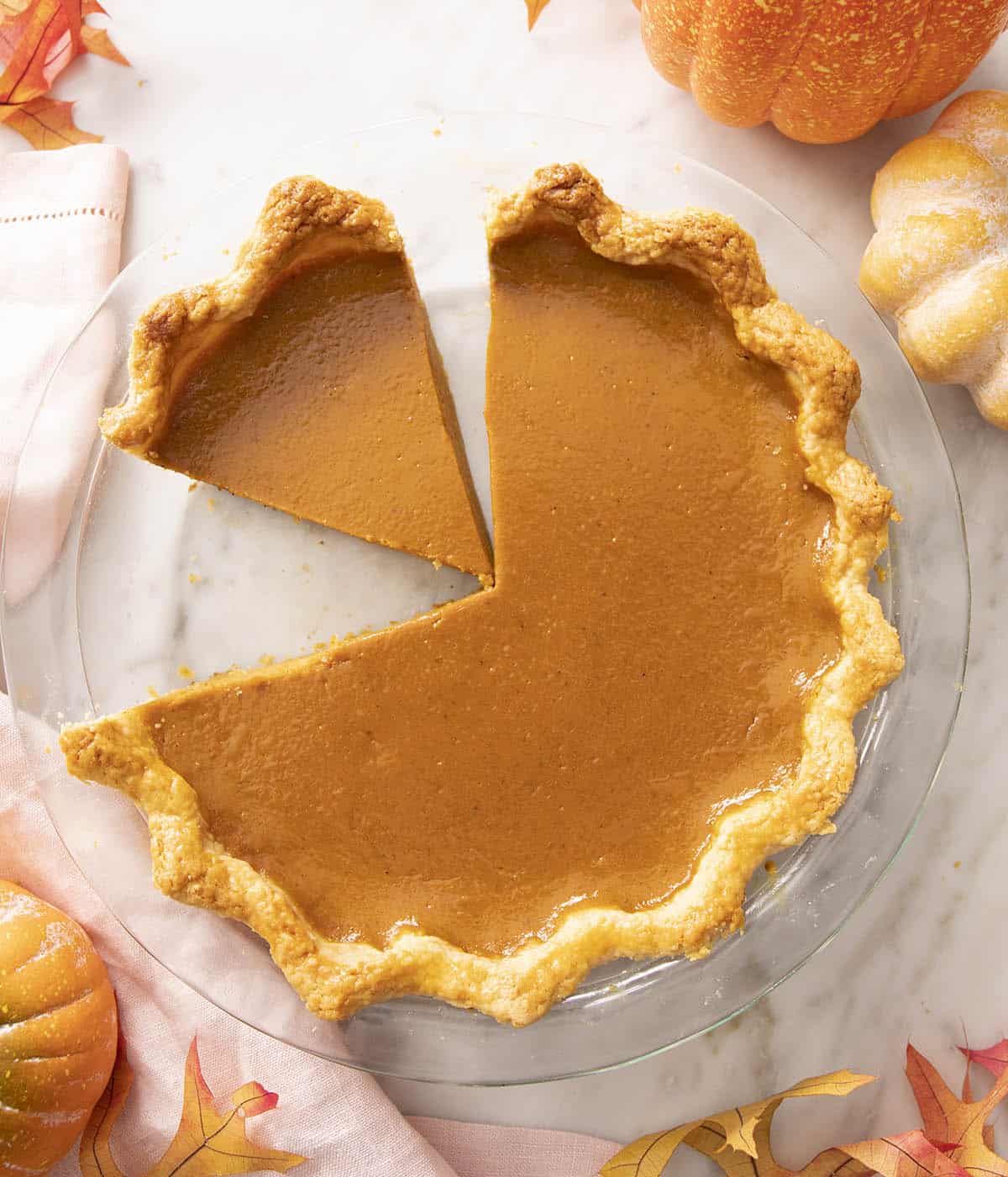 A pumpkin pie in a glass baking dish with a slice cut out.