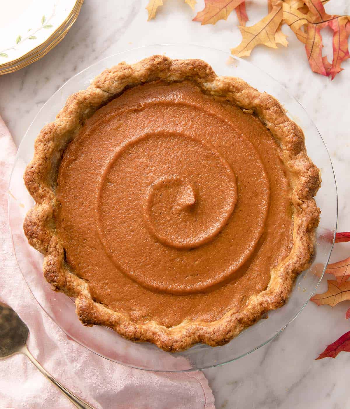 Whole sweet potato pie with a swirl on top in a glass pie dish.