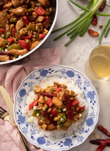 An overhead shot of Kung Pao chicken on a blue plate with a glass of wine beside it
