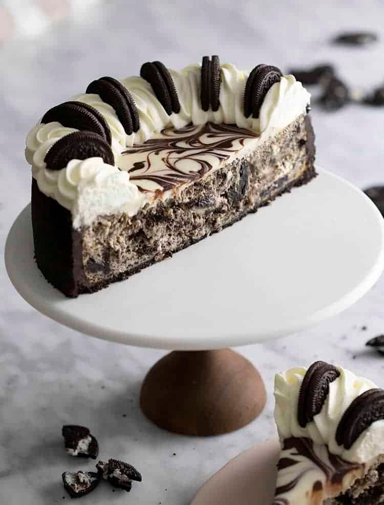 Half an Oreo cheesecake on white cake stand.
