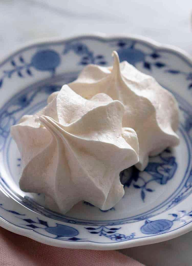 Two white meringue cookies on a porcelain plate.