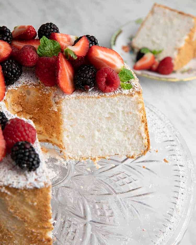 An angel food cake topped with fruit and with a slice removed.