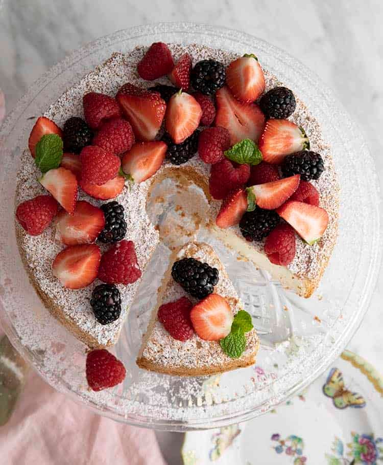 An overhead view of an angel food cake covered with fruit and powdered sugar.