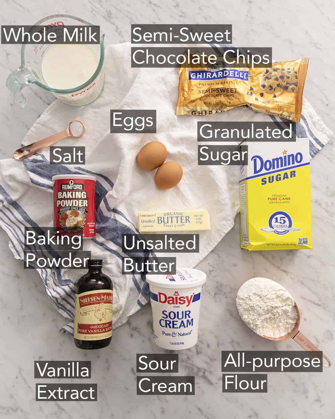 Ingredients to make chocolate chip muffins on a marble counter.